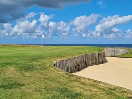 Un campo de golf con una bandera, búnkeres de arena y vista al océano.
