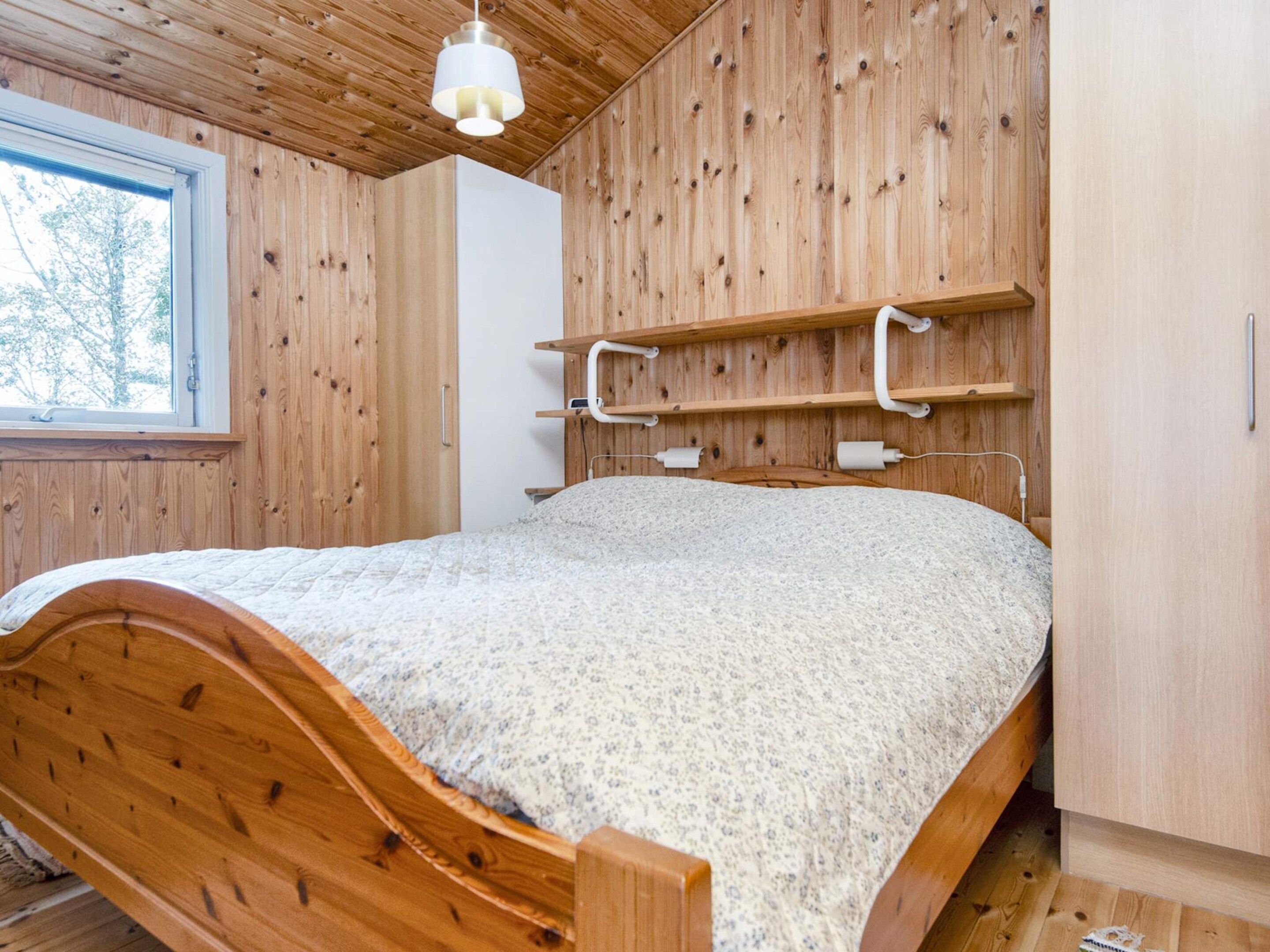 Un lit en bois avec une tête de lit, une fenêtre et un mur en bois doté d’étagères.
