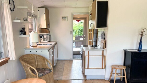 A compact kitchen with a dining area, a wicker chair, a small stool, and a view into the adjacent room. - 6 Person Holiday Home in Struer (Struer)