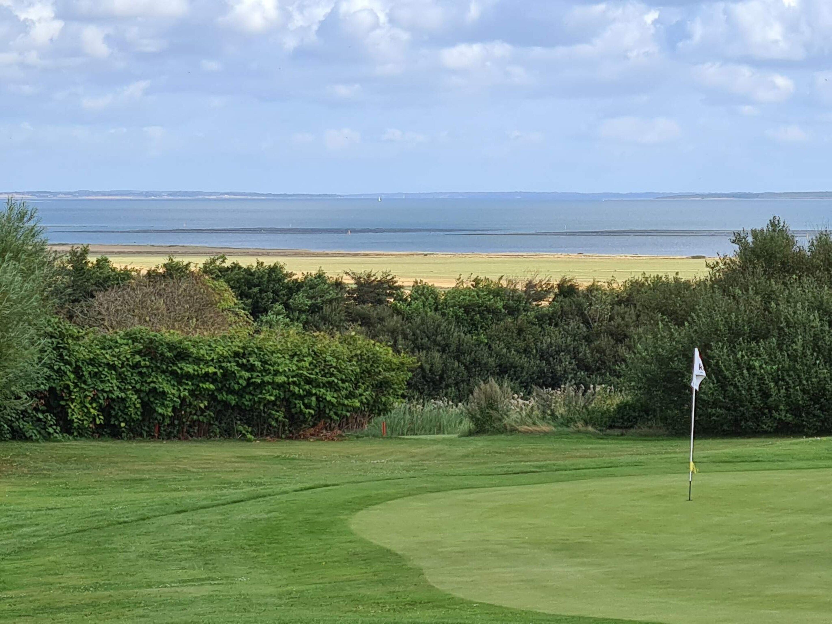 Een golfbaan met een vlag, een zandstrand en uitzicht op zee.