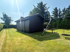 A black metal shed with a ladder, a swing set, and a well-maintained lawn.