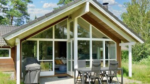A covered outdoor seating area with a table and chairs, a grill, and a view of the interior. - 5 Star Holiday Home in Asnaes (Asnaes)