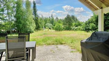 An outdoor patio with a covered seating area, a grill, and a view of a grassy field with trees.