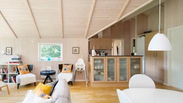 Amplia sala de estar con techo alto, paredes de madera, una mesa de comedor y una zona de cocina con armarios de madera.