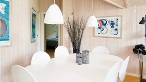 A dining area with a round table, white chairs, pendant lights, and artwork on the walls. - 5 Star Holiday Home in Asnaes (Asnaes)