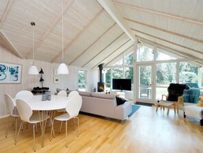 A spacious living area with a high ceiling, a fireplace, a television, and a large window offering a view of the outdoors.