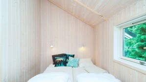 A small, cozy room with wooden walls, a single bed with white bedding, two wall-mounted lights, and a window with a view of greenery. - 5 Star Holiday Home in Asnaes (Asnaes)