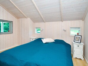 A bedroom with a large bed, two bedside tables, a window, and a small window.