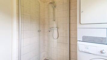 Un baño con ducha, inodoro y lavadora.