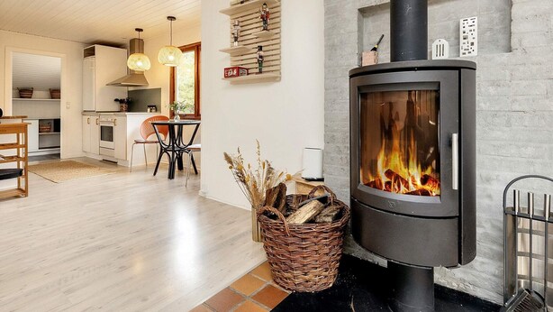 A modern kitchen with white cabinets, a dining area with a table and chairs, and a wood-burning stove. - 8 Person Holiday Home in Oksbol (Oksbol)