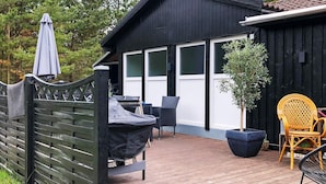 A wooden deck with outdoor furniture, a covered grill, and a black building with white trim. - 8 Person Holiday Home in Oksbol (Oksbol)