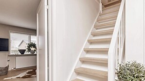 A modern interior with a wooden staircase, a white radiator, a window with blinds, and a potted plant. - 10 Person Holiday Home in Albaek (Aalbaek)