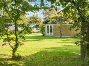 A residential area with a grassy lawn, a wooden fence, and a brick building with a glass door. - 8 Person Holiday Home in Skjern (Skjern)