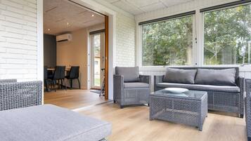 A modern living room with wicker furniture, a glass coffee table, and a view of the outdoors through large windows.