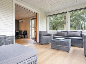 A modern living room with wicker furniture, a glass coffee table, and a view of the outdoors through large windows. - 8 Person Holiday Home in Skjern (Skjern)