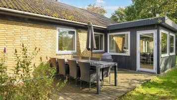A modern house with a patio area featuring a table and chairs, a deck, and a covered outdoor seating area.