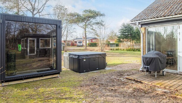 A modern outdoor living area with a hot tub, a covered barbecue, and a glass-enclosed structure. - 8 Person Holiday Home in Skjern (Skjern)