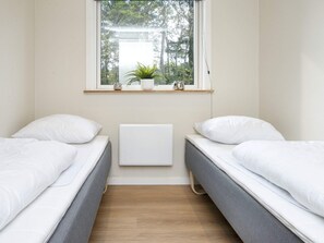 Une chambre avec deux lits simples, une fenêtre donnant sur des arbres, un radiateur et une étagère avec une plante et un vase.