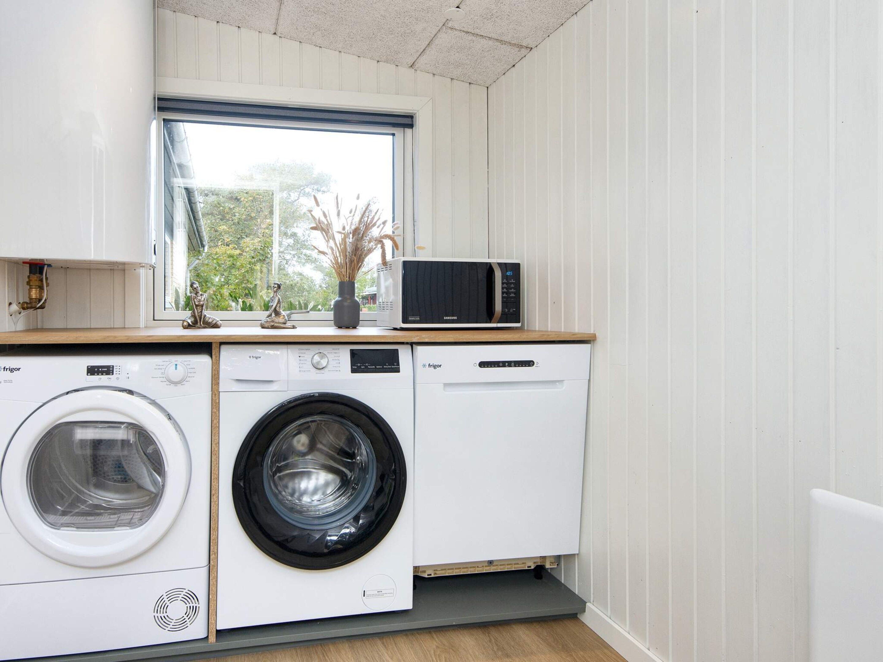 Een compacte keuken met een wasmachine, een magnetron en een raam boven de spoelbak.