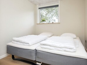A twin bed with white bedding, a small window with a plant, and a grey upholstered bench. - 8 Person Holiday Home in Skjern (Skjern)