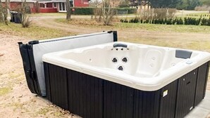 A hot tub with a black exterior and a white interior, placed on a concrete patio with a grassy area and a house in the background. - 8 Person Holiday Home in Skjern (Skjern)