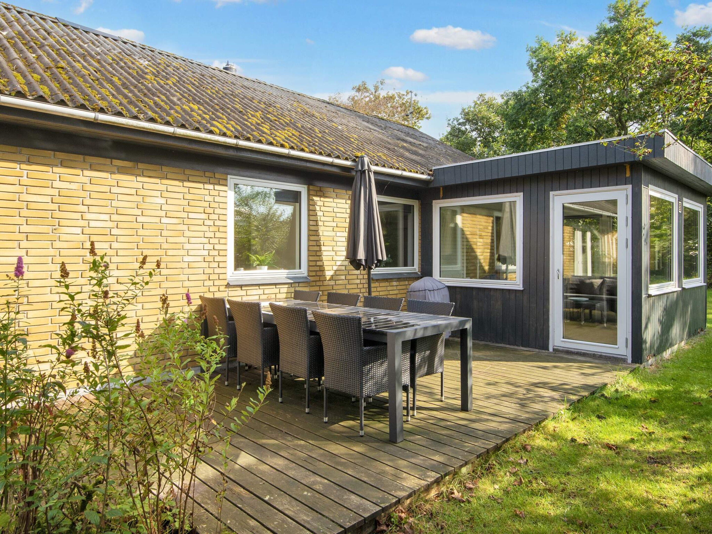 Ein modernes Haus mit einer Terrasse, einem Tisch, Stühlen, großen Fenstern und einer Holzterrasse.