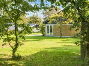 Un quartier résidentiel avec une pelouse verdoyante, une clôture en bois et un bâtiment en briques doté d’une porte en verre.