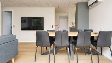 A modern dining area with a wooden table, black chairs, and a flat-screen TV mounted on the wall.