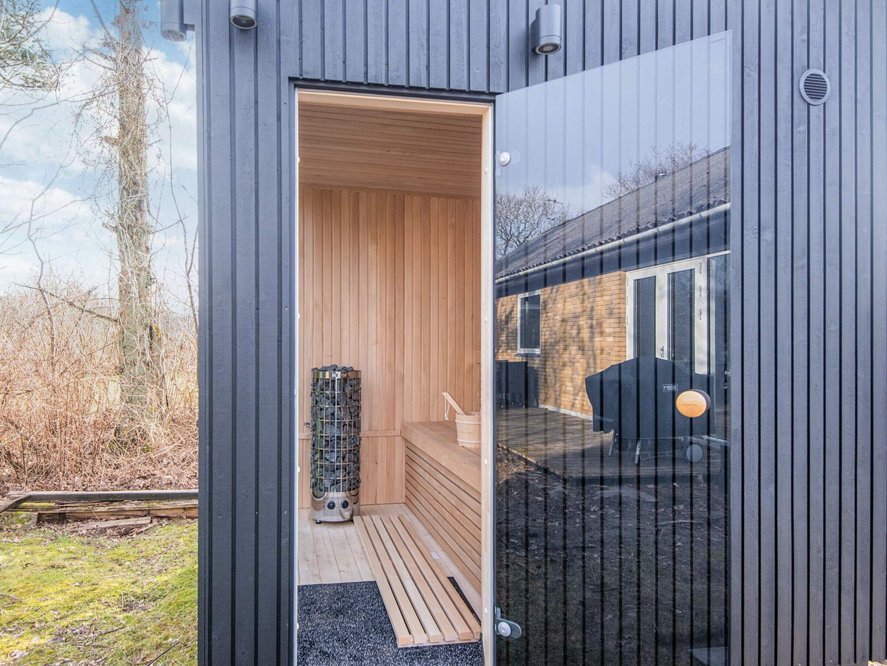 A modern sauna with a wooden interior, a glass door, and a metal sauna bench.