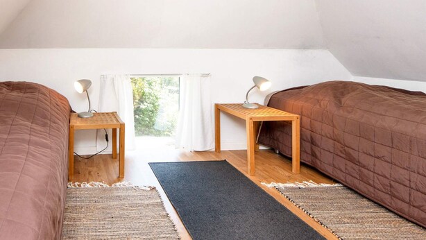 A room with two beds, a window with curtains, and a view of greenery outside. - 6 Person Holiday Home in Ringkobing (Ringkobing)