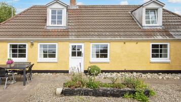 A yellow house with a tiled roof, a front door, and a small garden area with gravel and plants.