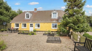 Una casa amarilla con un patio de grava, un banco de madera y una mesa de picnic.