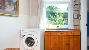 A laundry room with a washing machine, wooden cabinets, a window with curtains, and a painting on the wall. - 6 Person Holiday Home in Ringkobing (Ringkobing)