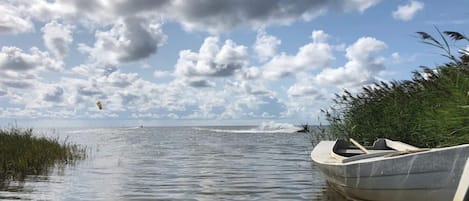 A calm body of water with a boat docked on the right, a grassy bank on the left, and a partly cloudy sky.