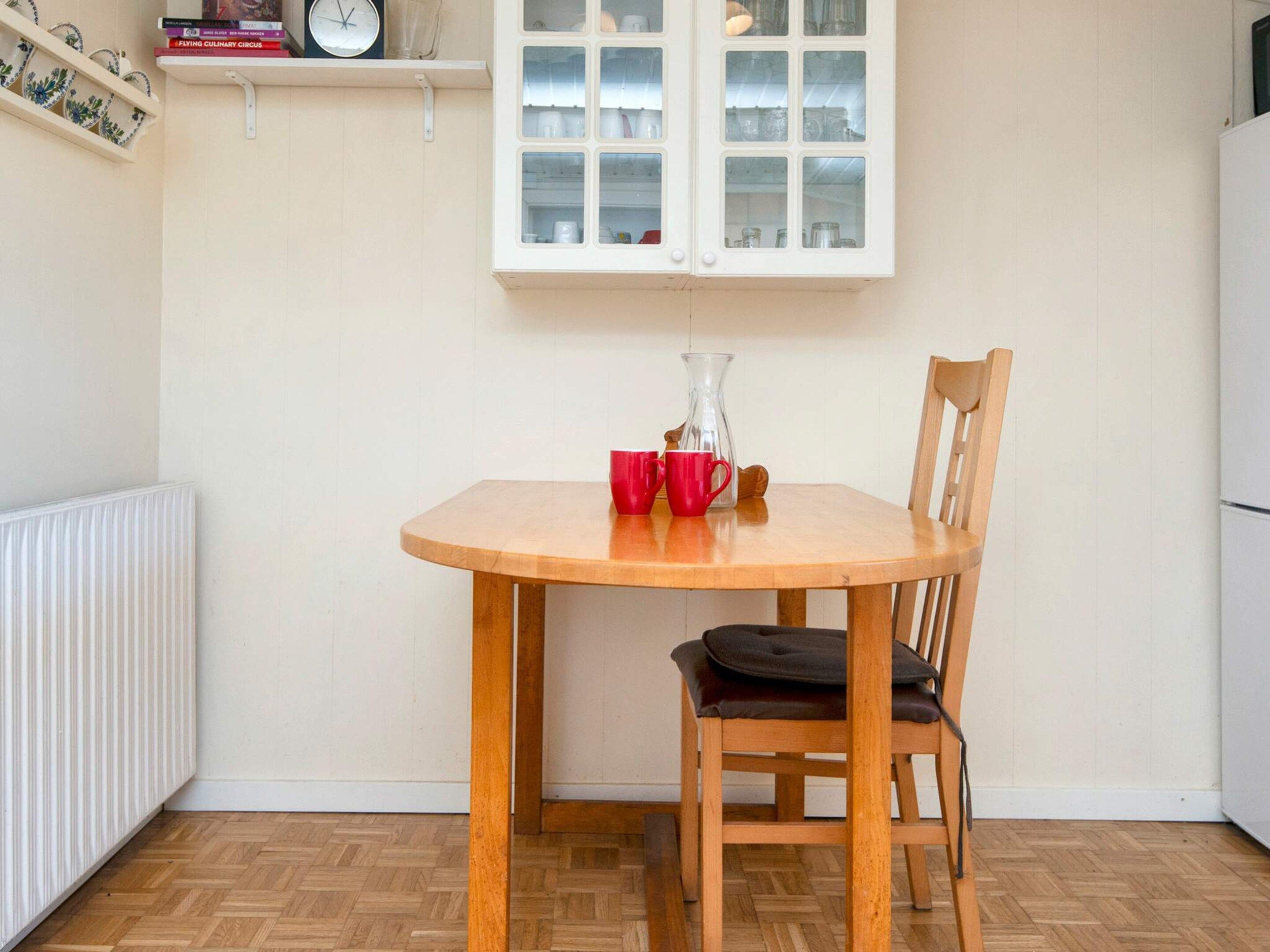 A small dining area with a wooden table and chair, a white cabinet above, and a radiator on the left.
