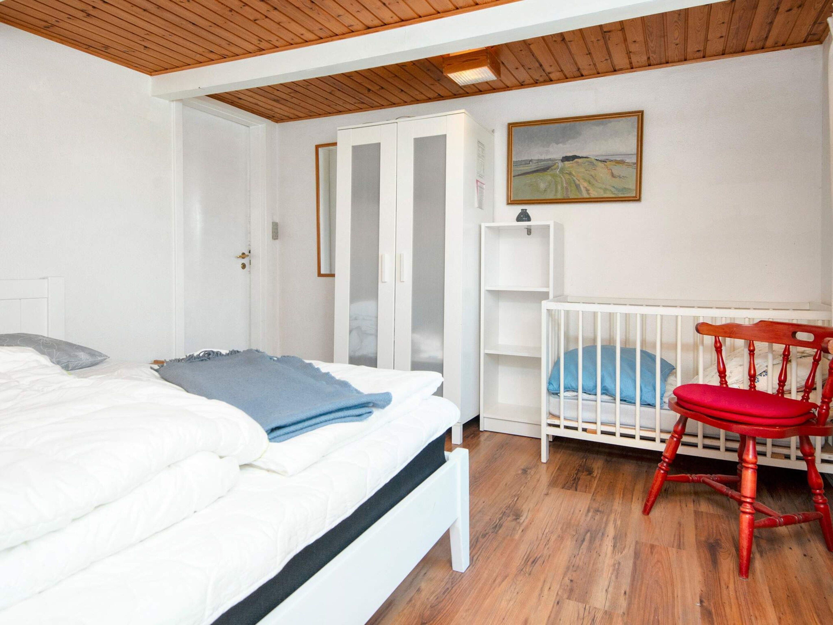 A bedroom with a bed, a crib, a wardrobe, and a painting on the wall.