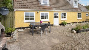 A yellow house with a tiled roof, a front door, and a patio with a table and chairs. - 6 Person Holiday Home in Ringkobing (Ringkobing)