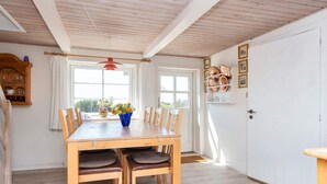 A dining area with a wooden table and chairs, a vase of flowers, and a view through the window. - 6 Person Holiday Home in Ringkobing (Ringkobing)