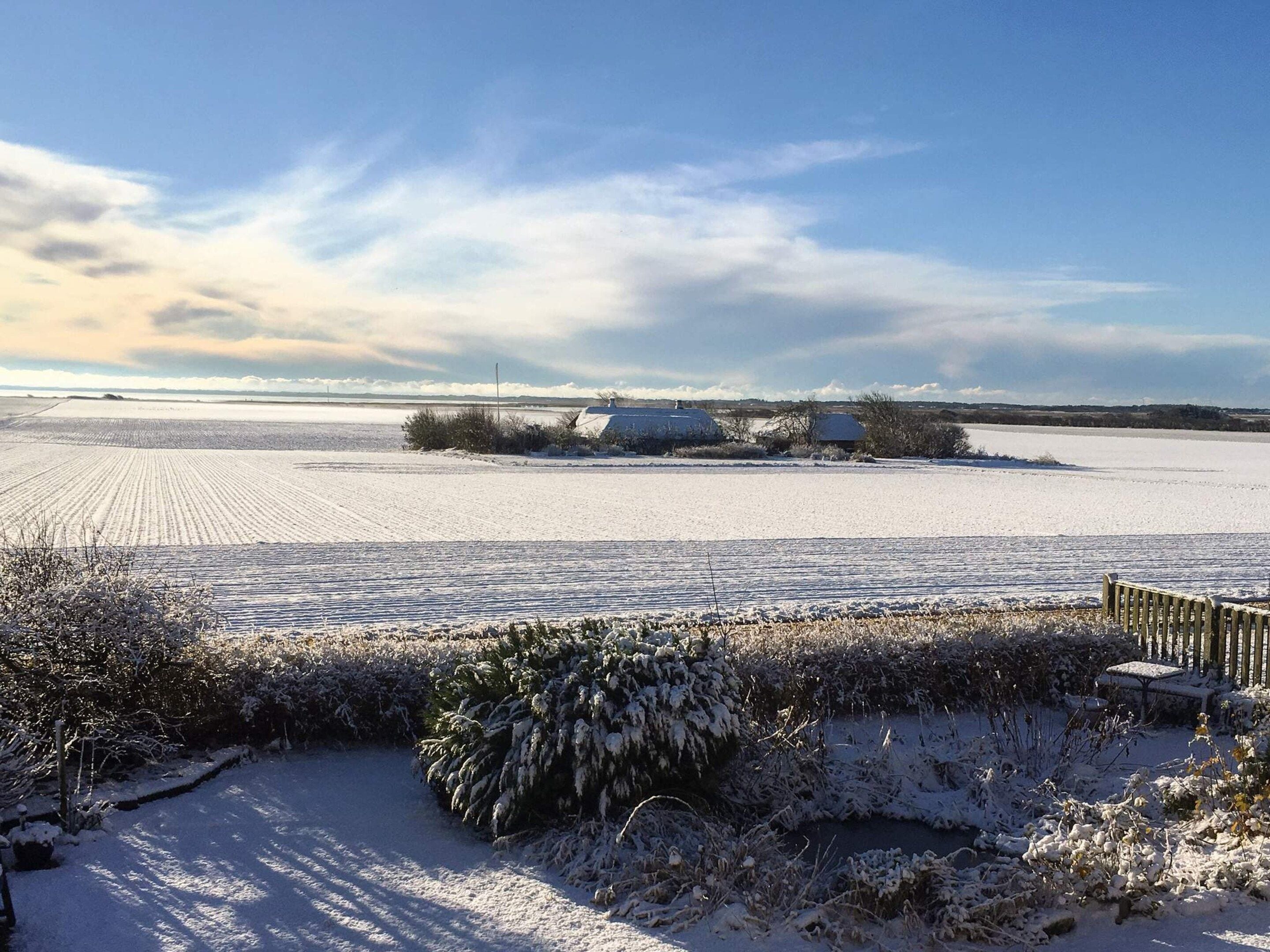 Eine verschneite Landschaft mit klarem Himmel, einem gefrorenen Feld und einigen Gebäuden in der Ferne.