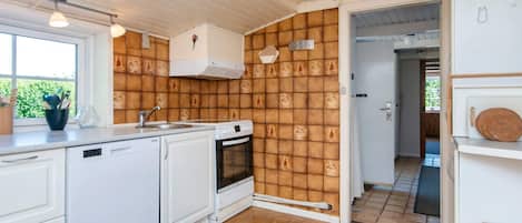 A kitchen with white cabinets, a stove, and a sink. There is a window with a view of greenery outside.