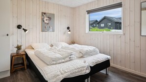 Une chambre avec un lit, une fenêtre donnant sur un beau paysage, une lampe fixée au mur et une petite table sur laquelle est posée une plante.