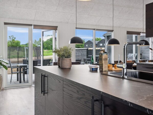 A modern kitchen with a large island, built-in appliances, and large windows offering a view of the outdoors.