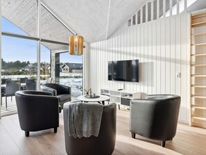 A modern living room with a large TV, comfortable seating, and a view of the outside.