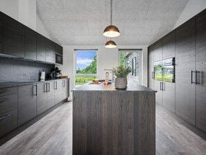 A modern kitchen with a central island, dark wood cabinets, and a view of greenery outside.
