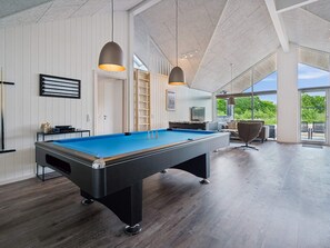 Una mesa de billar en una habitación amplia con techo alto y ventanas grandes.