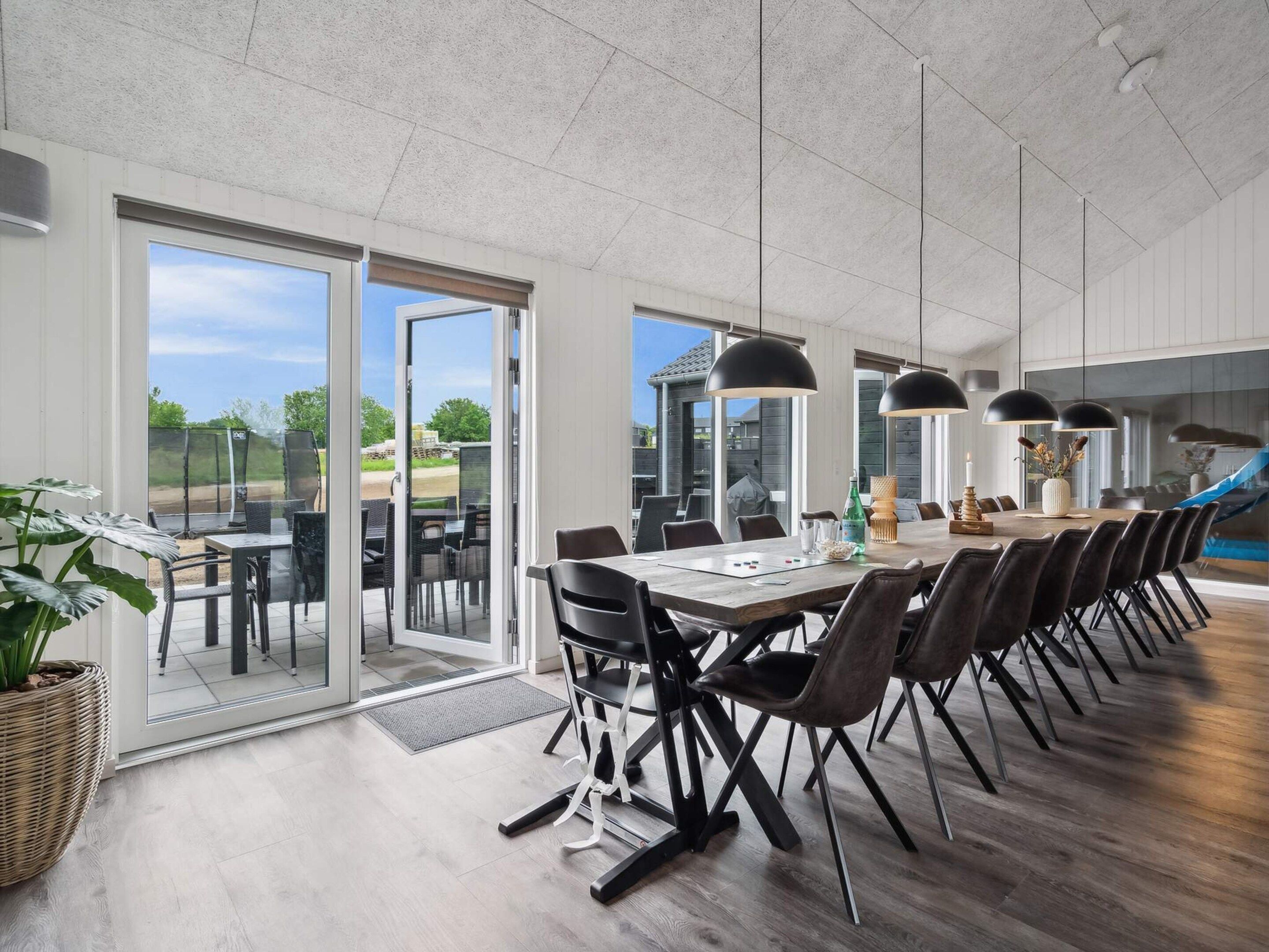 A modern dining area with a long table, chairs, and pendant lights.