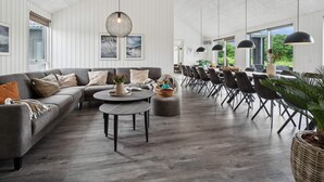 Un vaste espace de vie comprenant un canapé gris, une table basse ronde et un coin repas avec une longue table et des chaises.