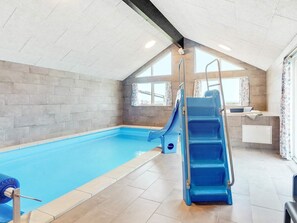 Una piscina interior con tobogán, vestuario y una ventana con cortinas.