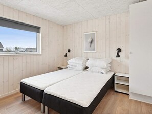 Un dormitorio con dos camas, una ventana, paredes de madera y un armario blanco.
