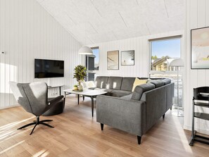 A modern living room with a grey sofa, a black armchair, and a coffee table. There is a flat-screen TV mounted on the wall, a potted plant, and artwork on the walls. - 5 Star Holiday Home in Sydals (Sydals)